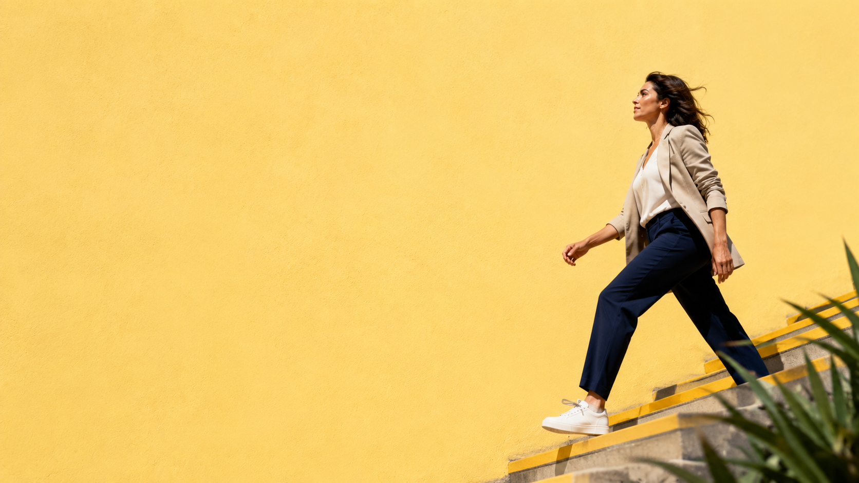 Editorial image of a professional woman walking upward on bright yellow steps against a vibrant yellow wall, representing the shift from useful production to confident ownership.